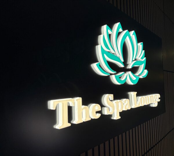 Illuminated sign displaying a stylized lotus flower above the words "The Spa Lounge" on a dark background.