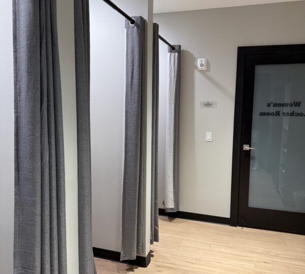 A row of changing rooms with gray curtains inside a retail store, next to a black door labeled "Women's Locker Room.
