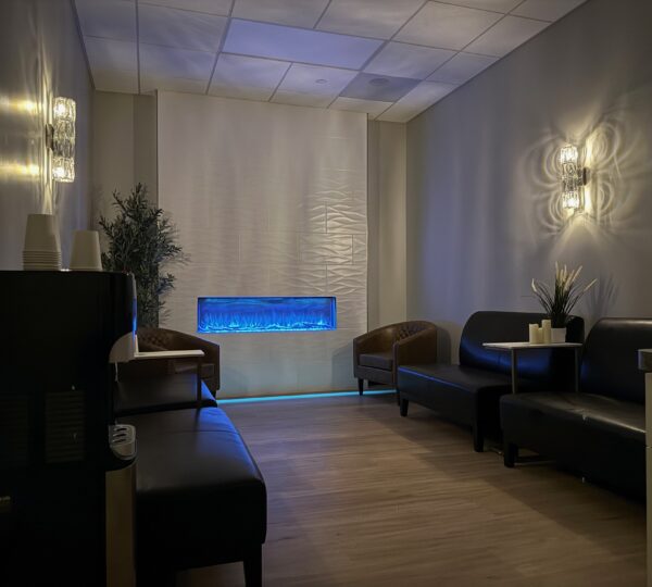 A dimly lit waiting room with black and brown seating, a blue-lit wall feature, plants, and a water dispenser on the left.