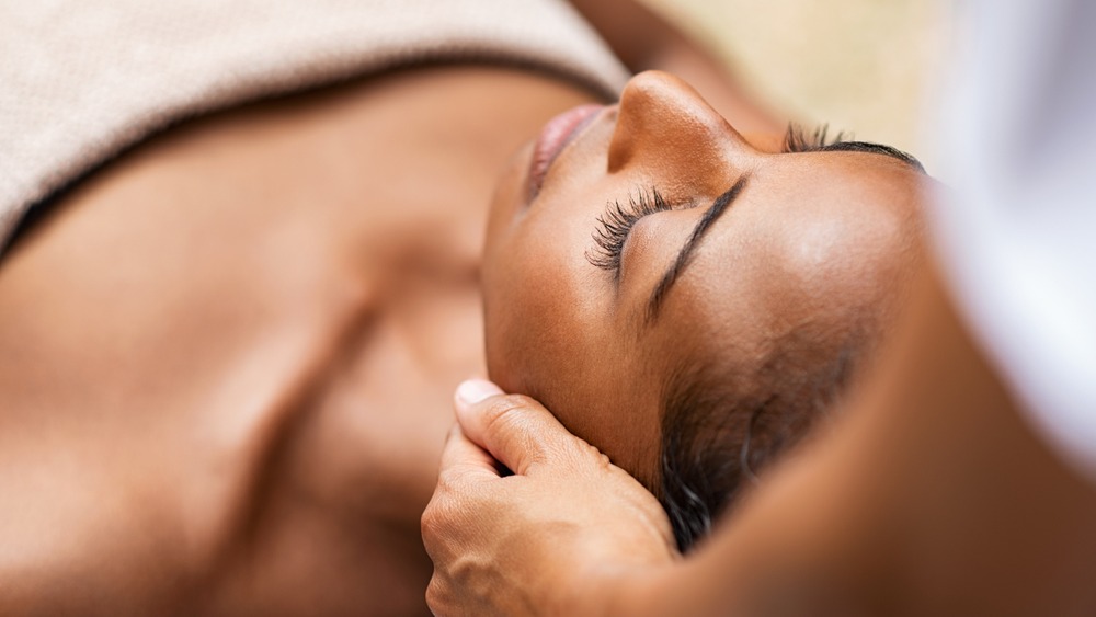 Person lying down with eyes closed while receiving a gentle neck massage, covered with a towel—a tranquil experience that’s often enjoyed in a Couples Massage session.